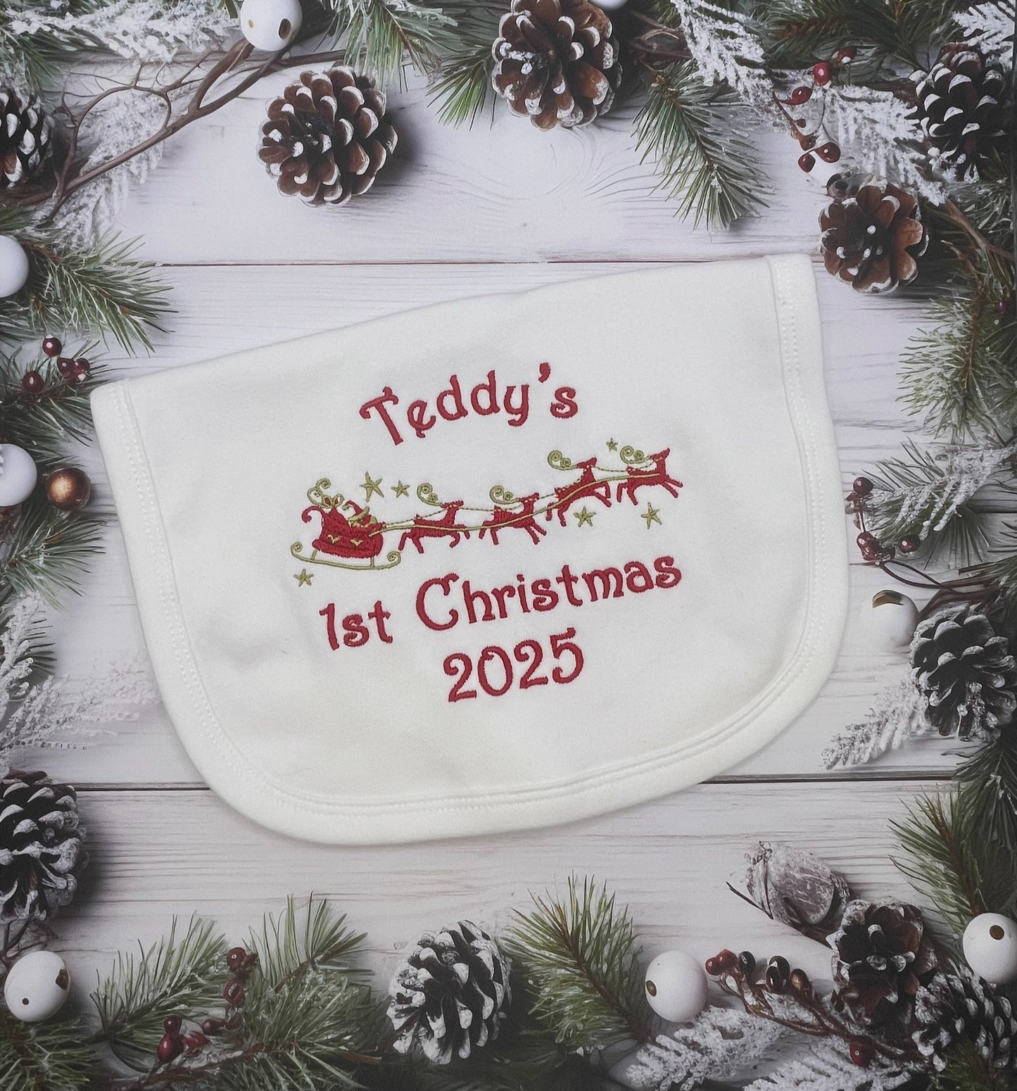 white baby bib with name and 1st Christmas 2025' text on a festive background