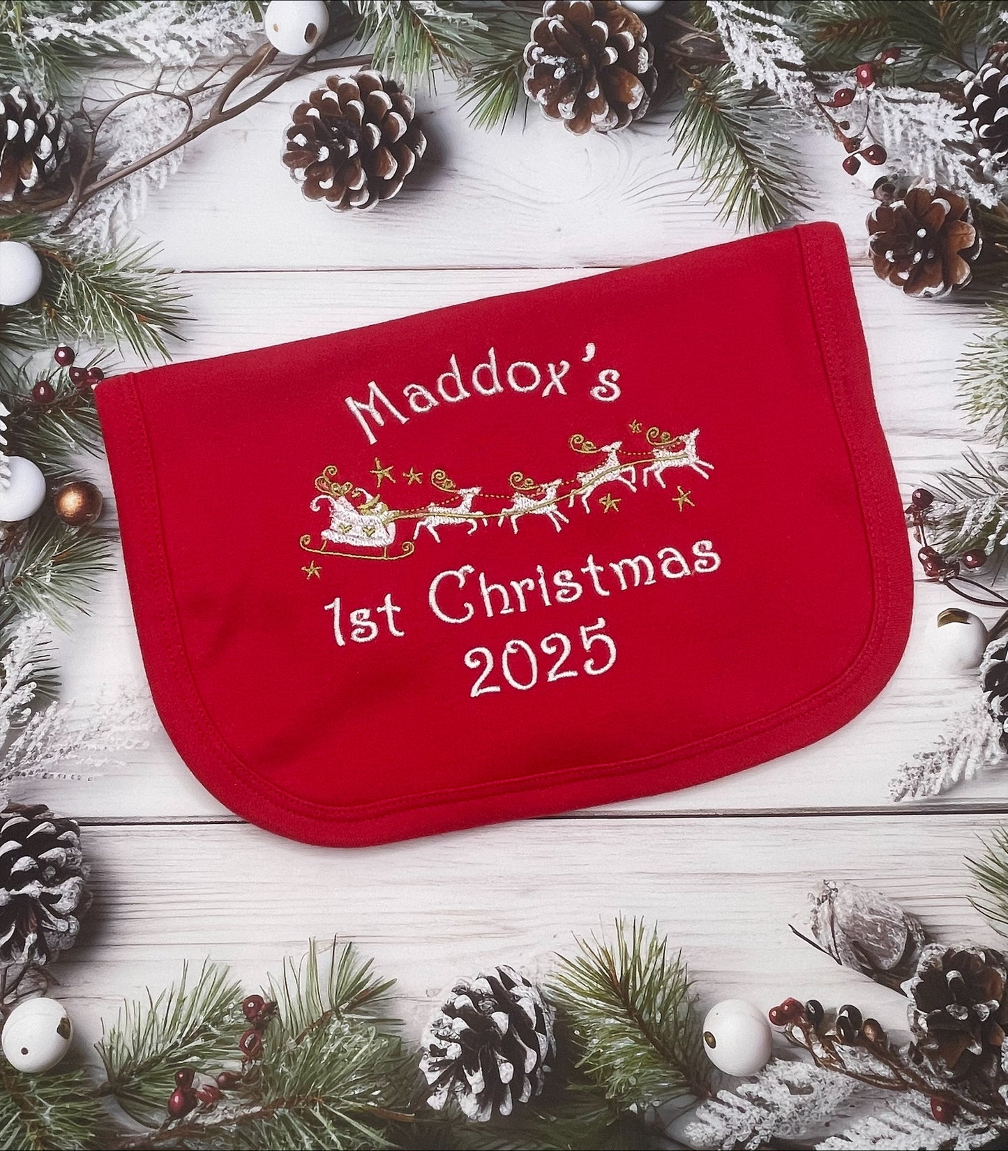 Red baby bib with name and 1st Christmas 2025' text on a festive background