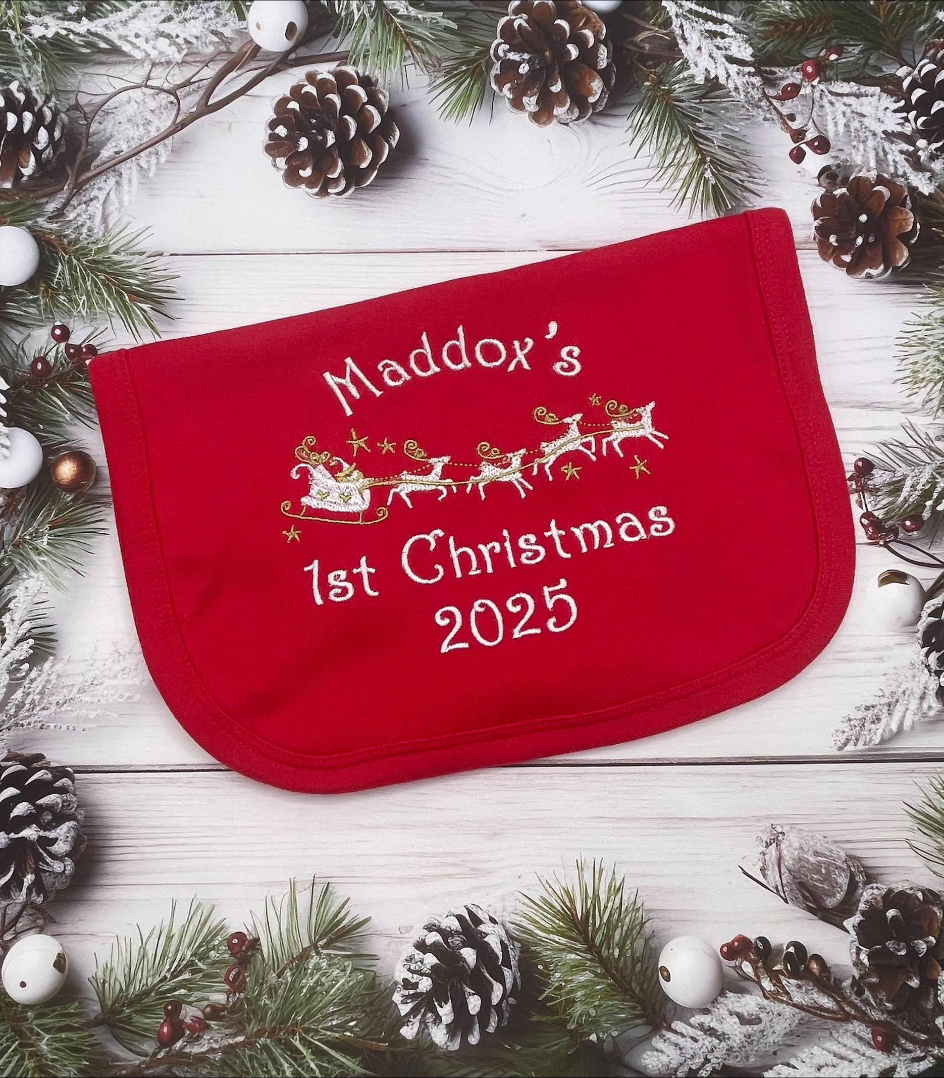 Red baby bib with name and 1st Christmas 2025' text on a festive background